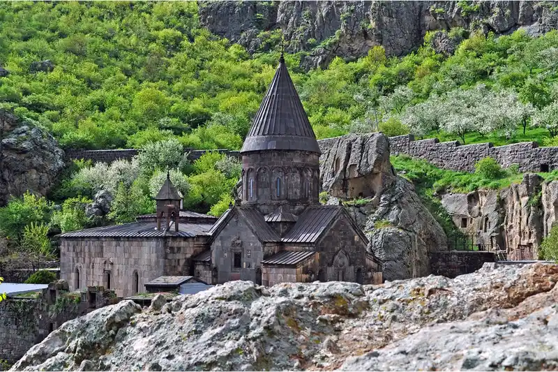 تصویر صومعۀ سنگی گغارد میان کوه‌های سرسبز و صخره‌ای ارمنستان